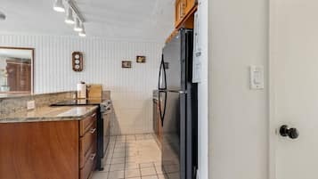 A kitchen with white tiled walls, wooden cabinets, a black refrigerator, and a countertop with a sink and stove.