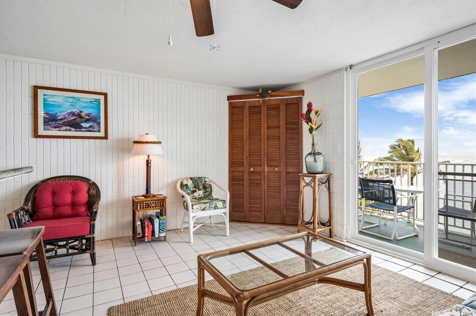 A room with a glass table, a red chair, a white chair, a wooden door, and a view of the ocean.