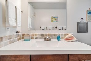 A bathroom with a white sink, a mirror, and a towel rack. There is a soap dispenser and a tissue box on the counter. - Luxury Oceanview Punaluu Condo (Hau`ula)