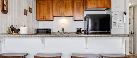 A kitchen with wooden cabinets, a black refrigerator, a microwave, and a coffee maker. There are three wooden stools at the counter.