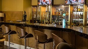 Zona de bar con mostrador de mármol, varias botellas de licor y dos televisores mostrando una imagen borrosa.