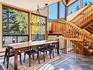 A dining area with a wooden table and chairs, a chandelier, and a view of trees through large windows. - Ski shuttle to Deer Valley, hot tub and sauna (Park City)