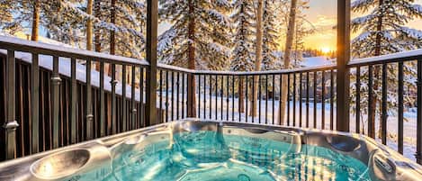 A hot tub with a view of snow-covered trees and a sunset.