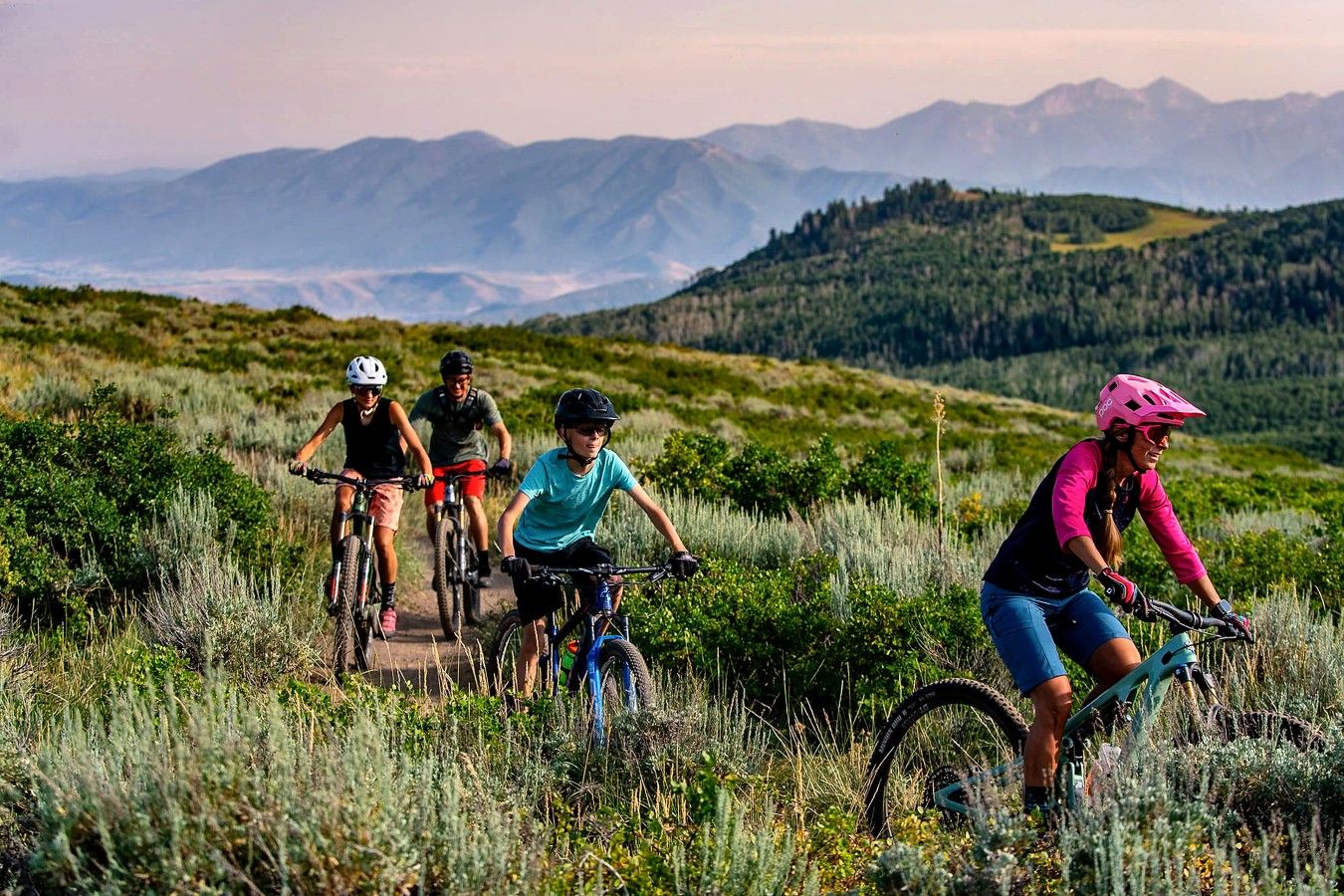 A group of cyclists on a trail with a mountainous backdrop.