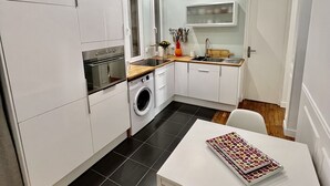 Une cuisine de taille réduite, avec des meubles blancs, un lave-linge, un évier et une table sur laquelle est posé un magazine.