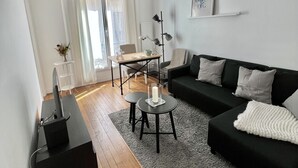 Un salon moderne avec un canapé noir, une petite table basse, un bureau avec un ordinateur et une lampe sur pied.