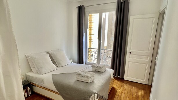 Une chambre à coucher avec un lit, une fenêtre avec des rideaux et un plancher en bois.