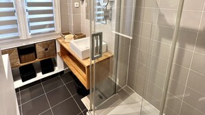 Une salle de bain moderne avec une douche à parois de verre, un meuble-lavabo et une fenêtre équipée de stores.