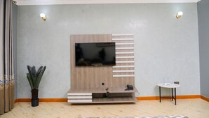 Una sala de estar con un televisor de pantalla plana montado en un mueble de madera, una mesita y una planta en maceta.