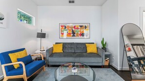 Una sala de estar moderna con un sofá gris, un sillón azul y una mesa de centro de vidrio.