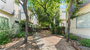 Un patio con un sendero curvo, rodeado de árboles y vegetación, que conduce a la entrada de un edificio.