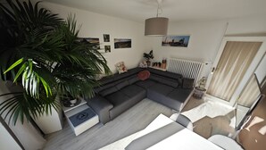 A modern living room with a sectional sofa, a dining table, and a large potted plant. - Familienfreundliche Ferienwohnung in Wernigerode, mit Eigenem Garten (Wernigerode)
