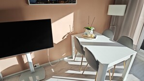 A modern room with a flat-screen TV, a dining table with chairs, a potted plant, and a painting of a cityscape. - Familienfreundliche Ferienwohnung in Wernigerode, mit Eigenem Garten (Wernigerode)