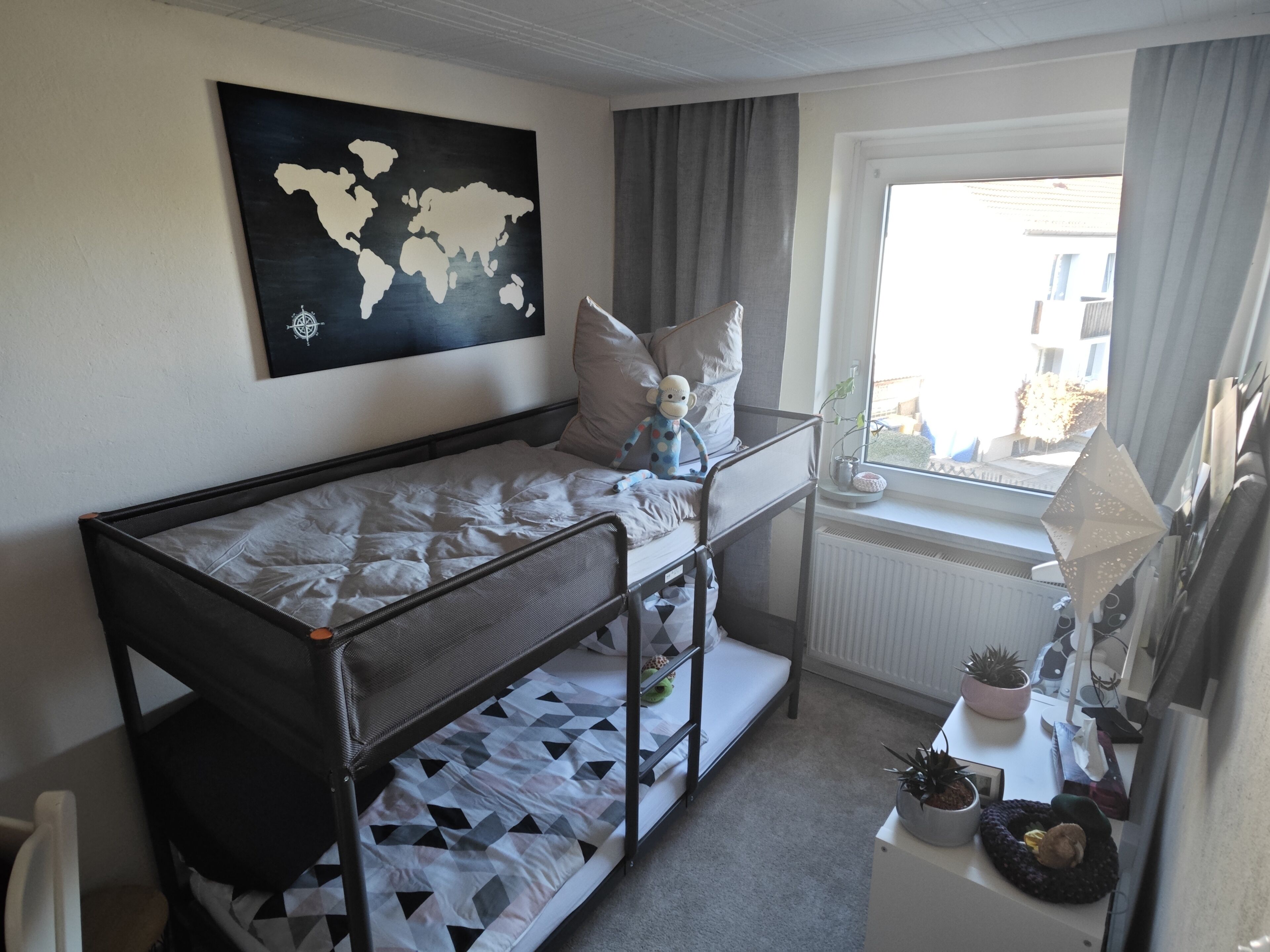Habitación con literas, un mapa del mundo en la pared, una ventana con cortinas y una pequeña mesa con plantas.