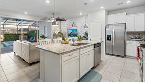 A modern kitchen with white cabinets, a stainless steel refrigerator, and a large island with a sink.