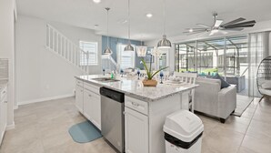 A modern kitchen with a central island, built-in dishwasher, pendant lighting, and a ceiling fan.