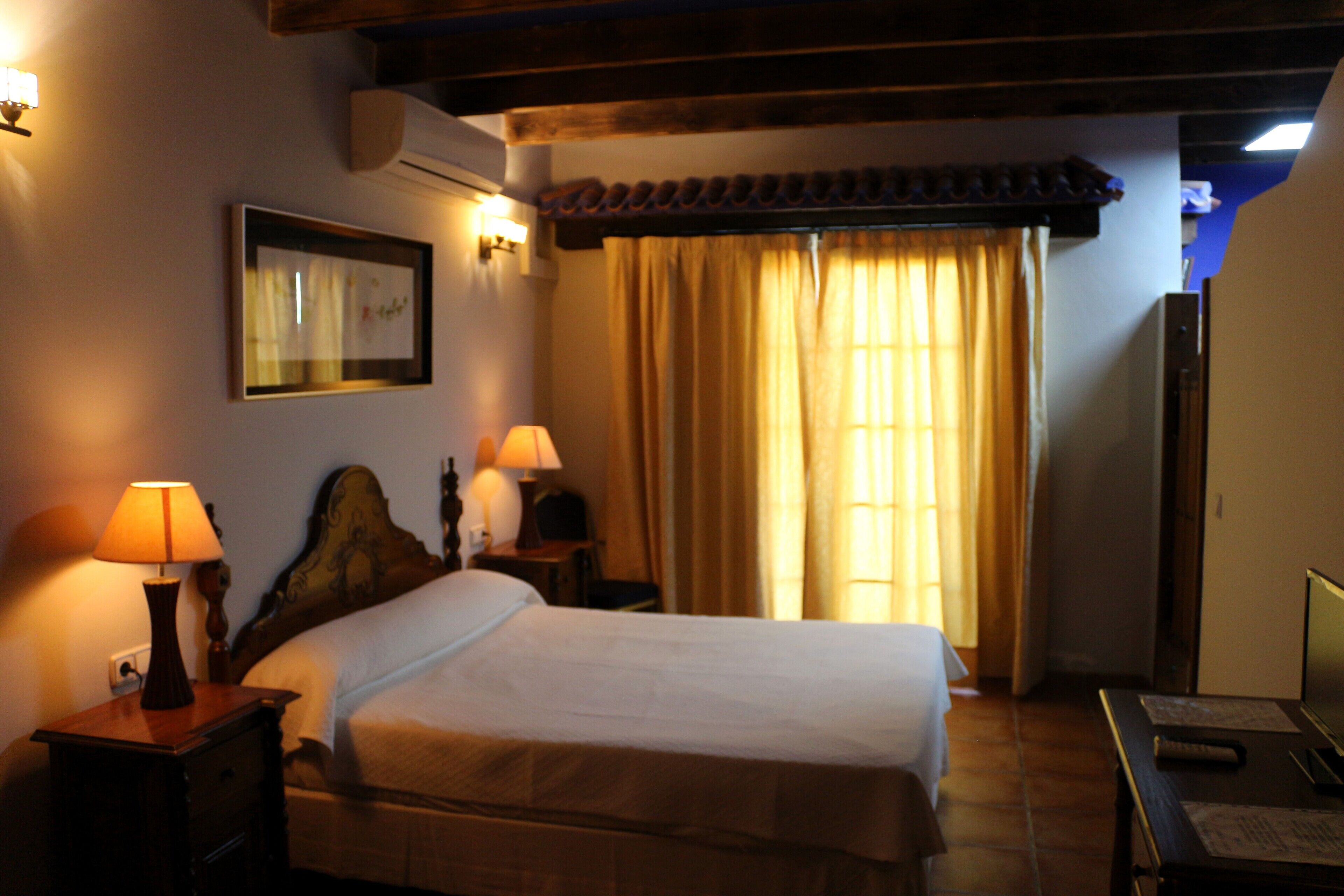 Een hotelkamer met een bed, twee nachtkastjes met lampen, een lijst aan de muur en een raam met gordijnen.