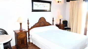 Un dormitorio ordenado con una cama de madera, dos mesitas de noche con lámparas, una silla e imagen enmarcada en la pared.