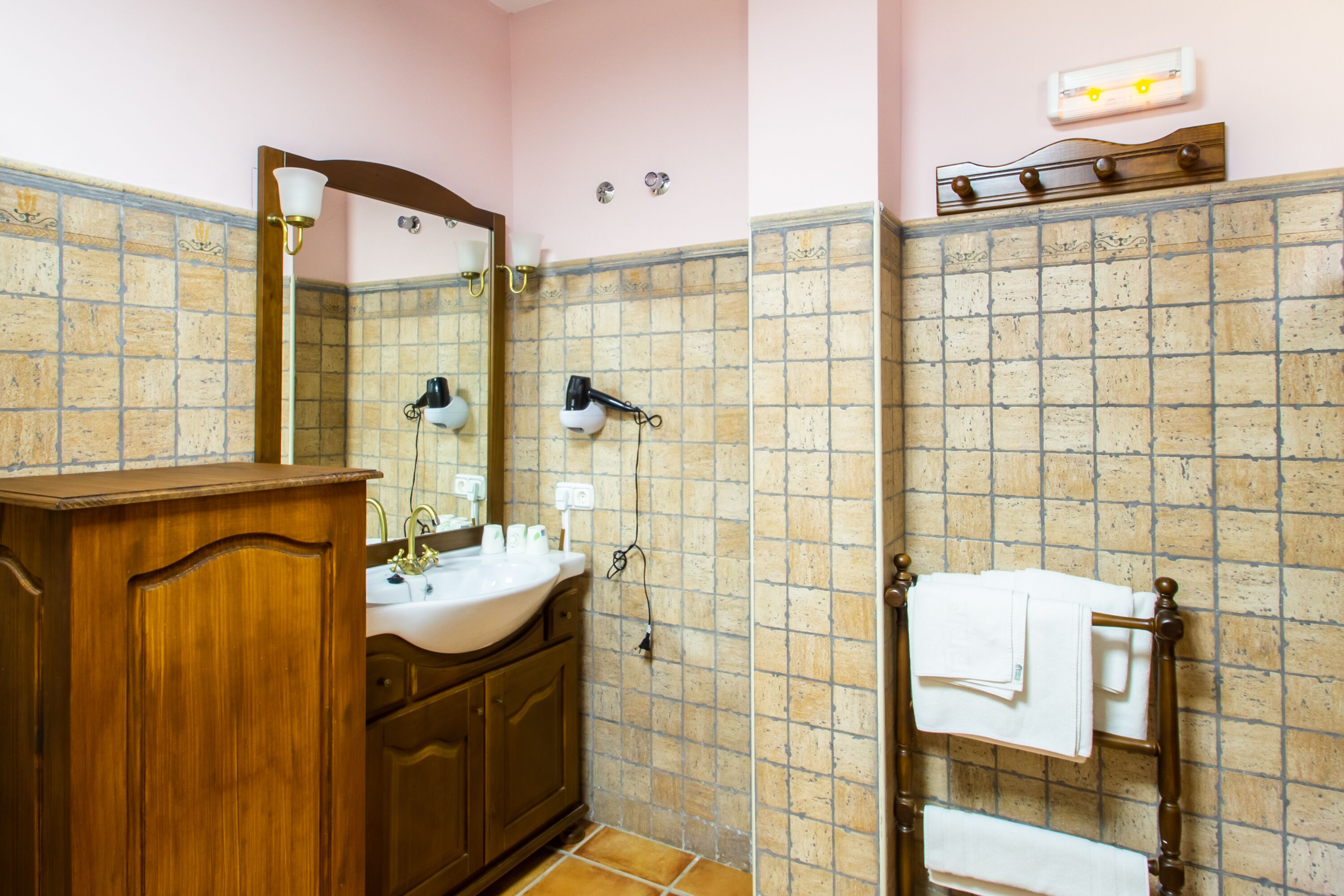 A bathroom with a wooden vanity, a sink, a mirror, a towel rack, and a shower area with a tiled wall.