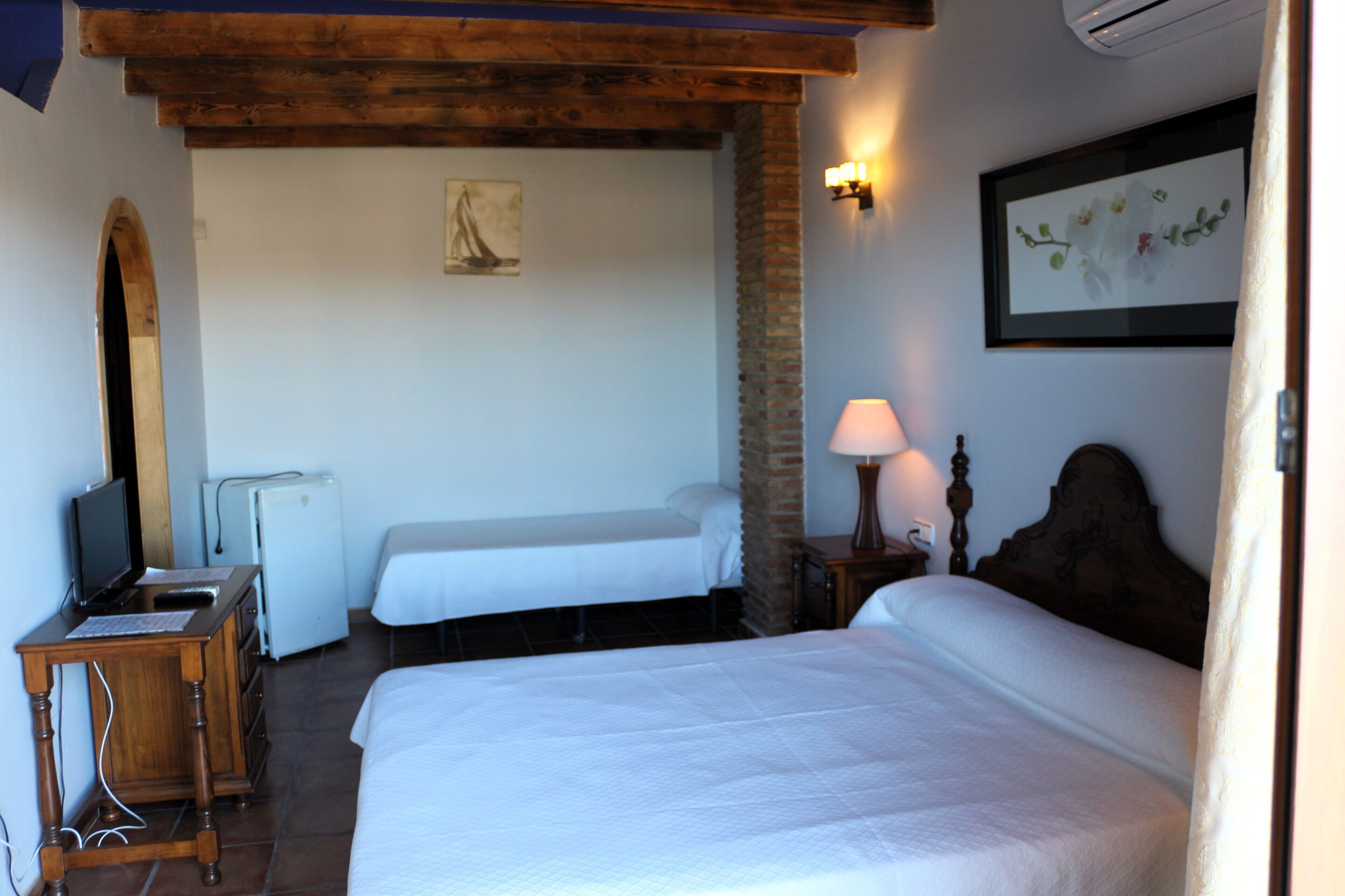 Una habitación de hotel con dos camas, un escritorio con computadora, un refrigerador y un televisor.