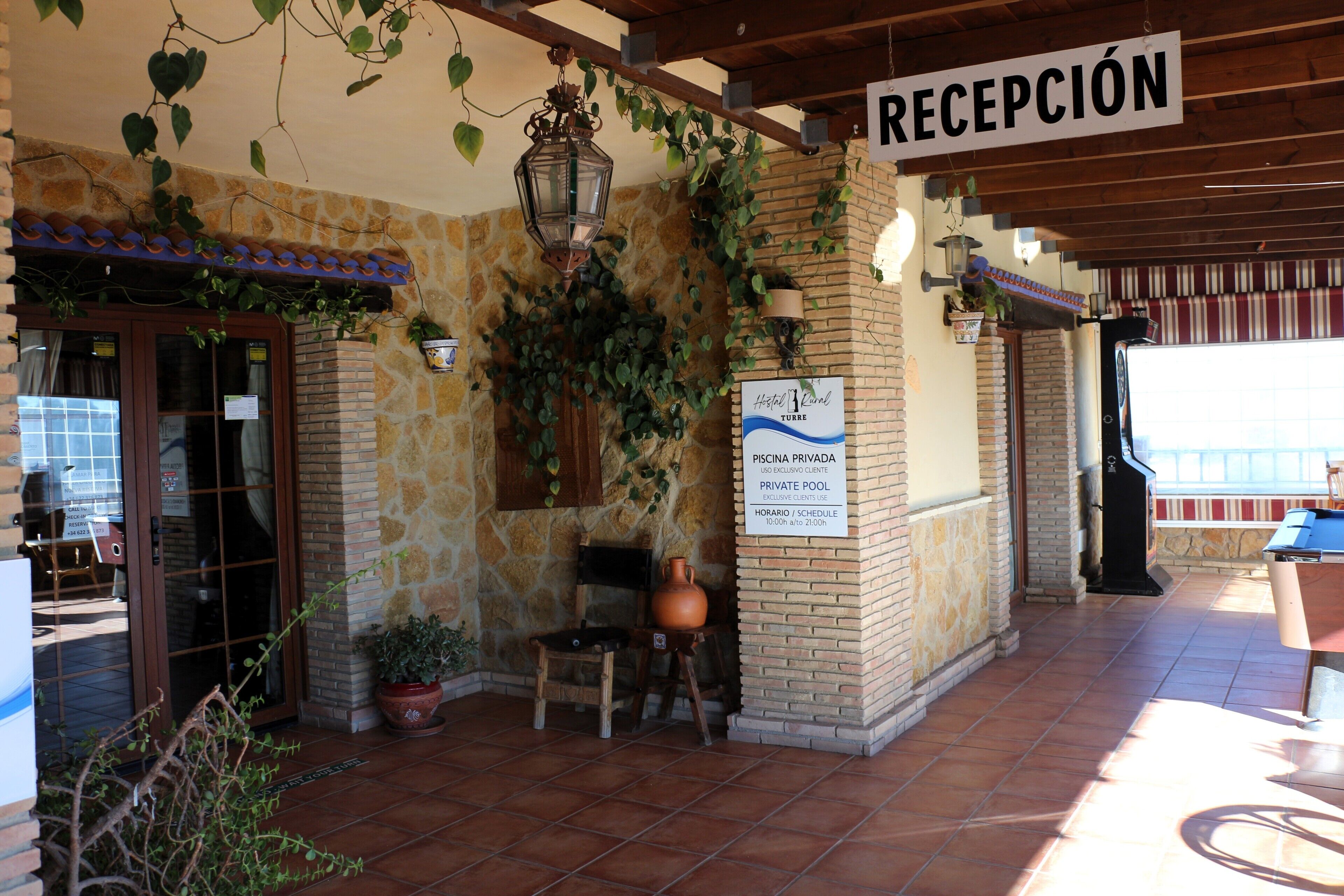 Un área de recepción con un letrero que indica piscina privada, pared de piedra, banco de madera y planta en maceta.