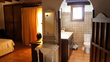 Un baño con lavabo, inodoro y espejo sobre el lavabo. Hay una ventana sobre el lavabo y una puerta que da a otra habitación.