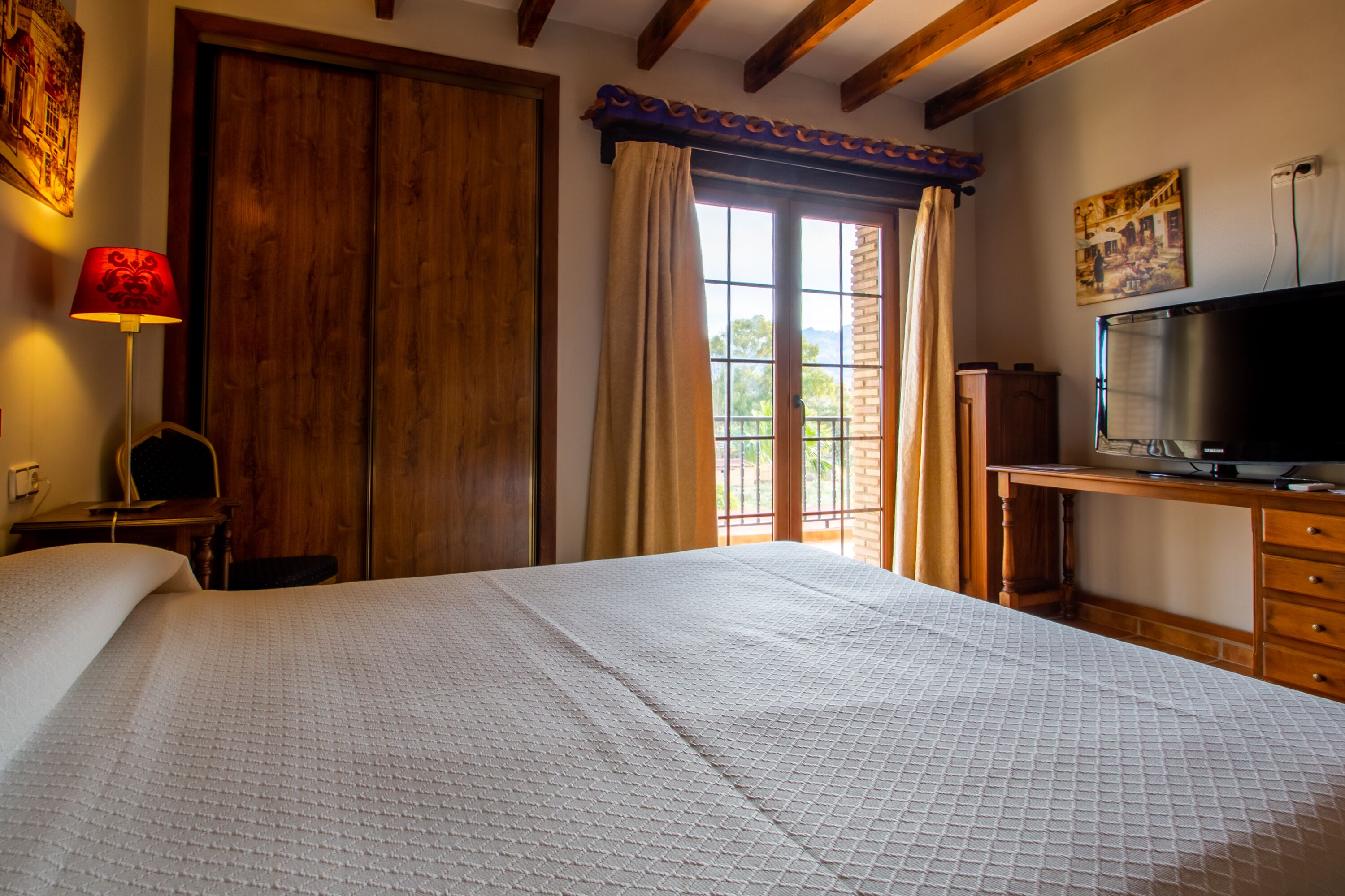 Un dormitorio con una cama grande, un armario de madera, un escritorio con televisor y una ventana con cortinas.