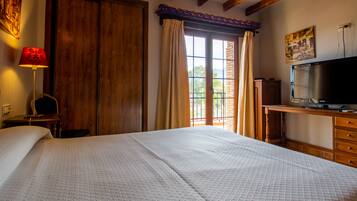 Un dormitorio con una cama grande, un armario de madera, un escritorio con televisor y una ventana con cortinas.