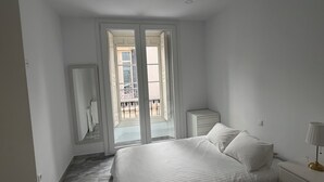Ein Schlafzimmer mit Bett, Nachttisch, Lampe, Spiegel und einem Fenster mit Blick auf einen Balkon.