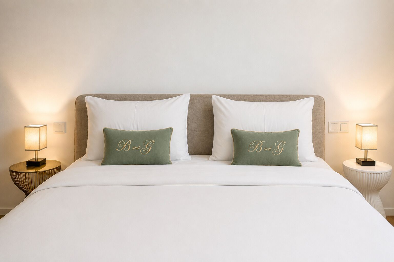 A bed with white bedding, two pillows with 'Band G' embroidery, and two bedside lamps.