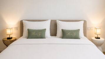 A bed with white bedding, two pillows with 'Band G' embroidery, and two bedside lamps.