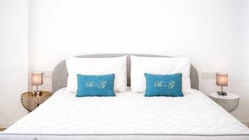Un letto con biancheria bianca, due cuscini blu con ricami e due lampade ai comodini su tavolini rotondi.