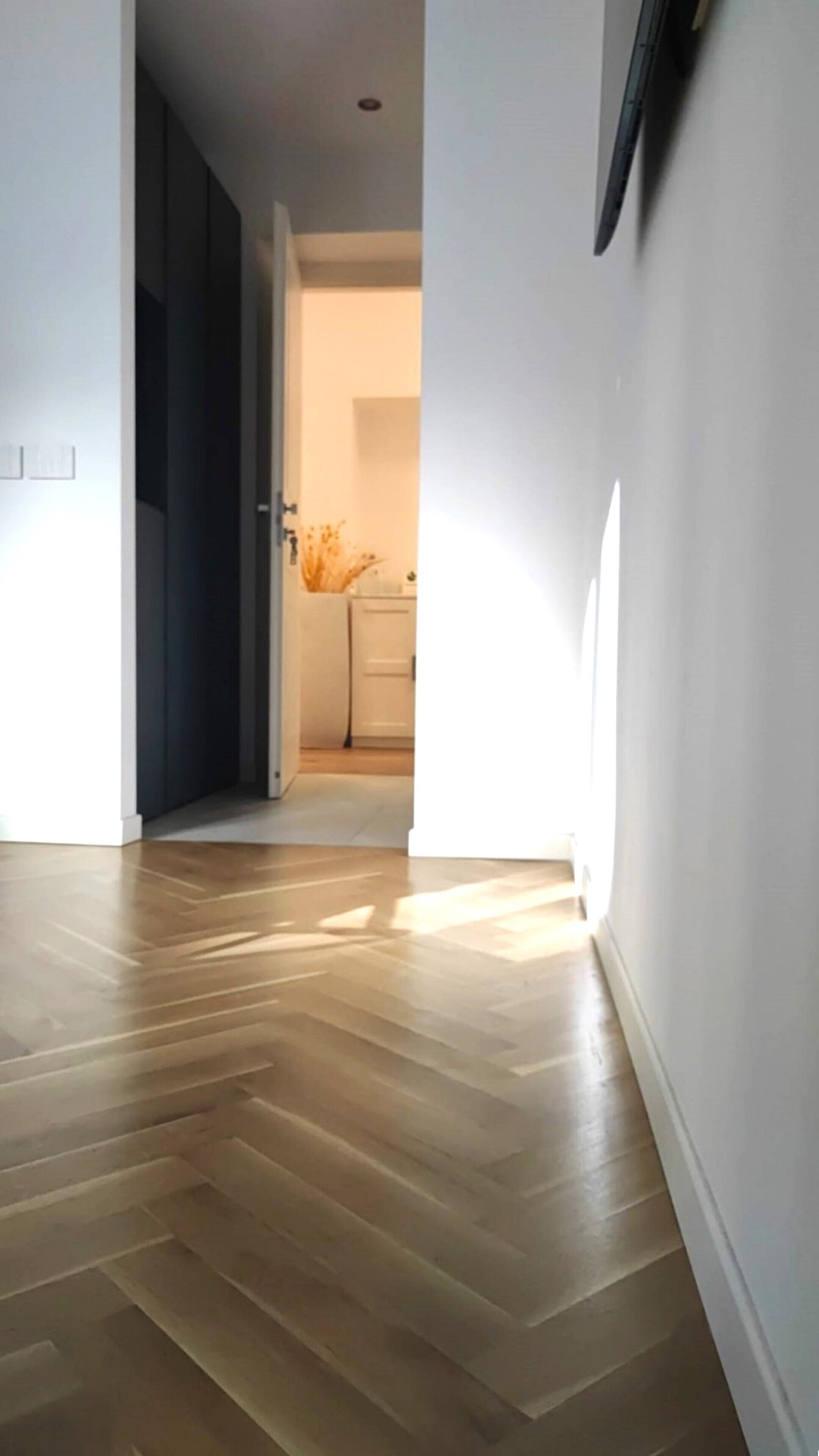 Un pasillo con piso de madera que conduce a una habitación con puerta blanca.