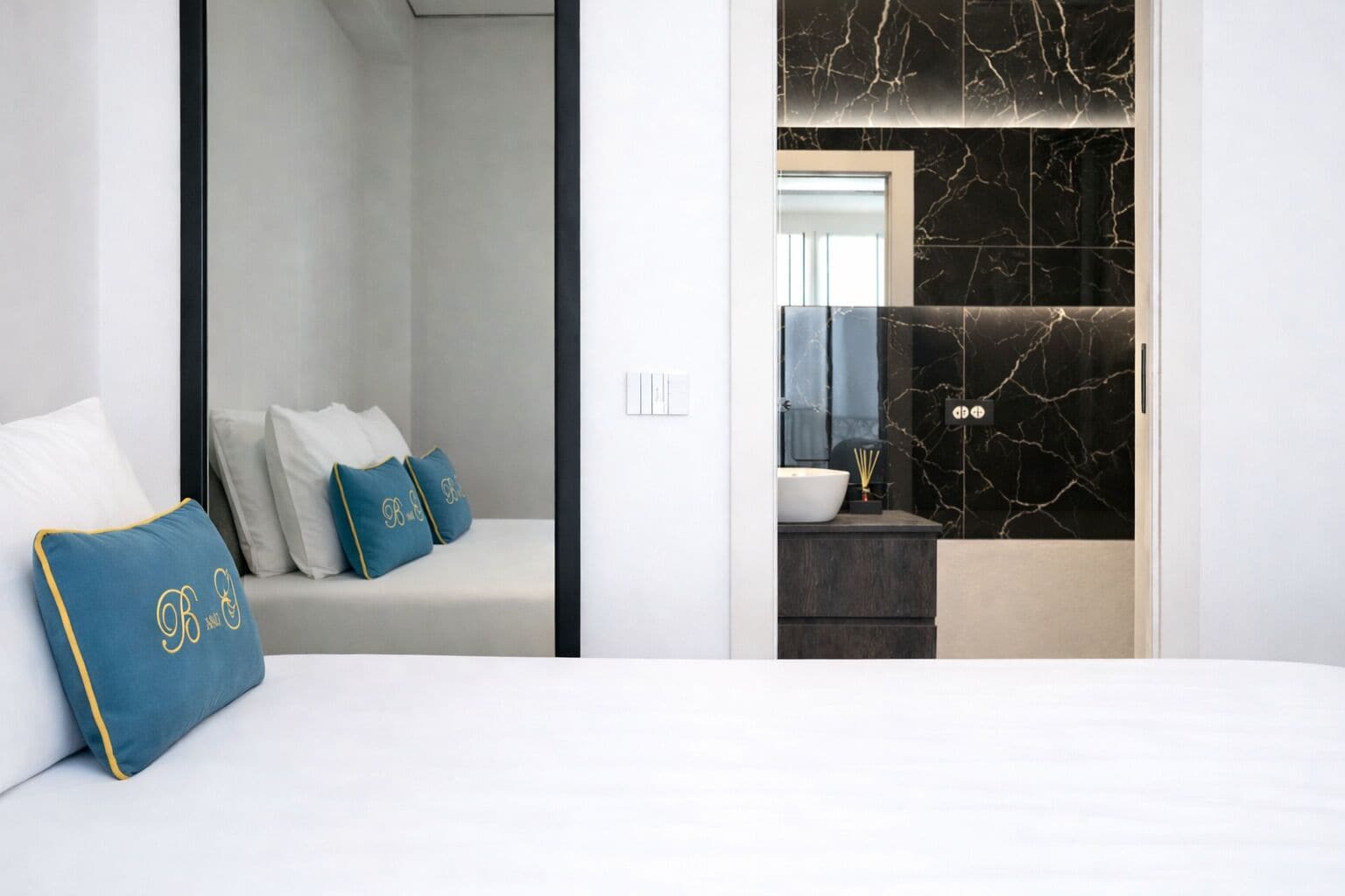 Ein modernes Hotelzimmer mit einem Bett, einer Couch mit dekorativen Kissen, einem Badezimmer mit Marmorverkleidung und einem Waschbecken.
