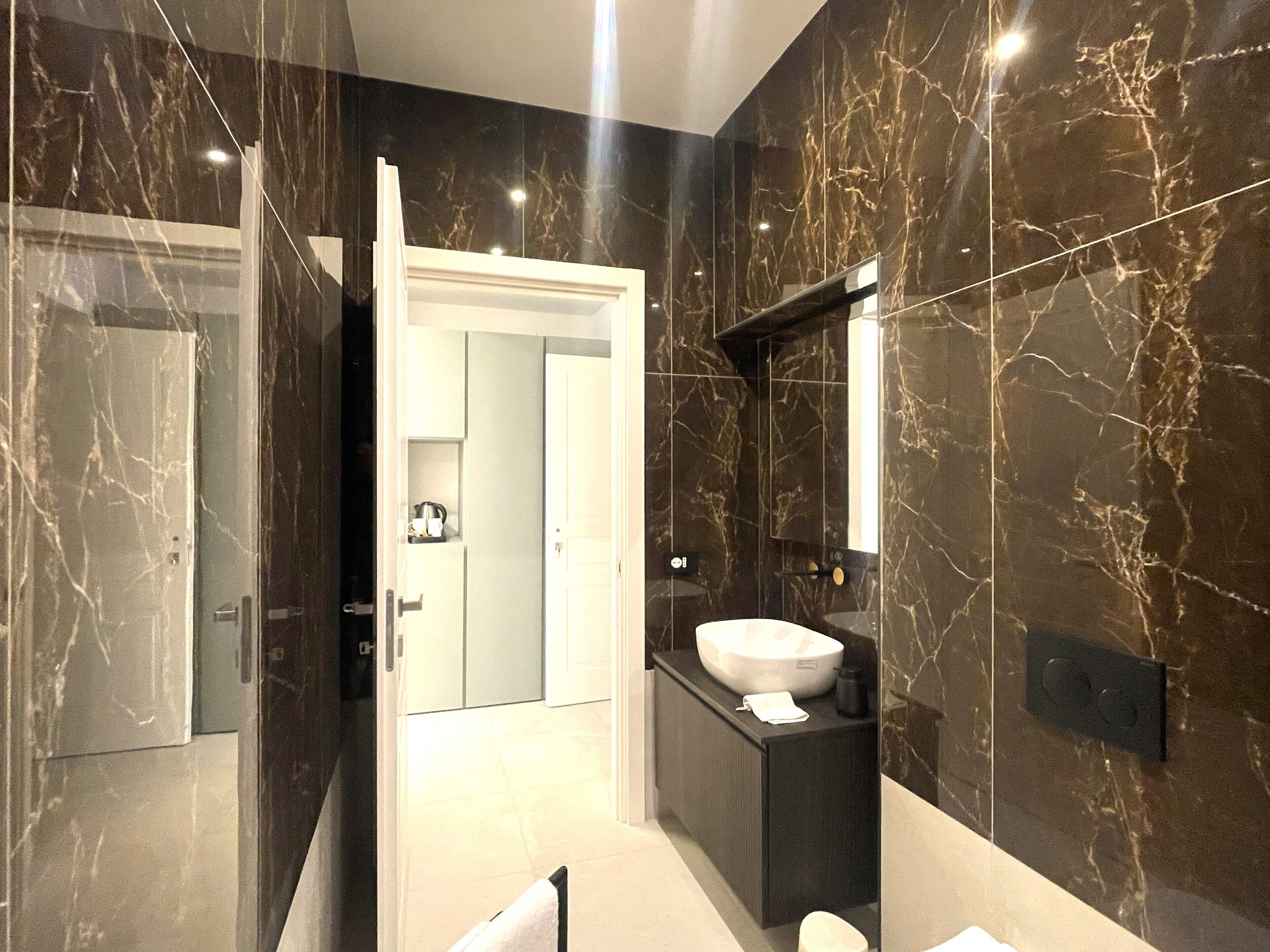 Une salle de bain moderne avec un meuble-lavabo en marbre, un grand miroir et une porte donnant sur une autre pièce.