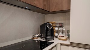 Une cuisine équipée d’une plaque de cuisson à induction noire, d’une machine à café et d’un présentoir pour les tasses et un panier.