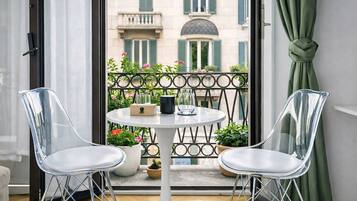 A balcony with a table and two chairs, a view of buildings, and a curtain.