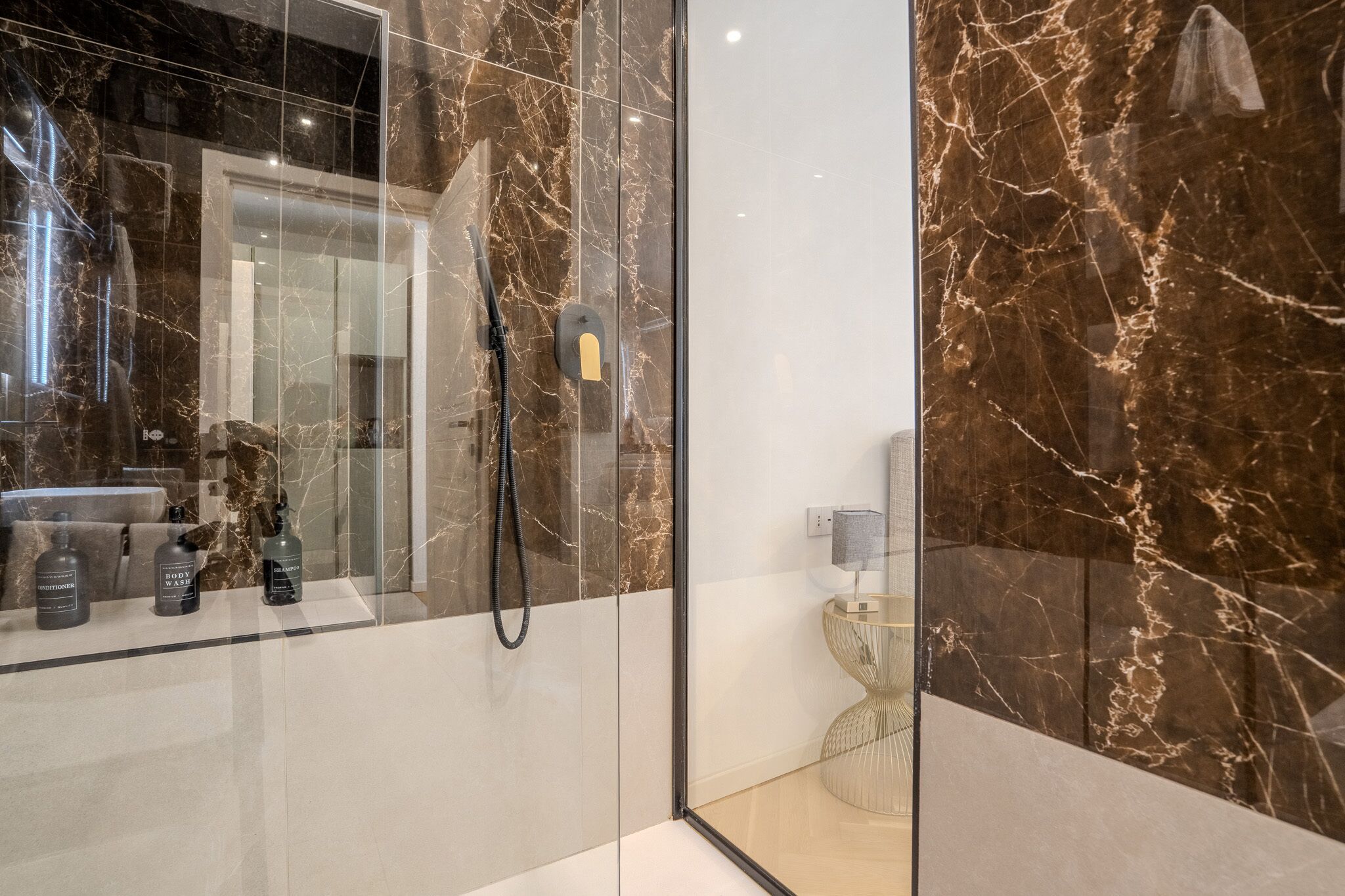 Un baño moderno con ducha de vidrio, paredes de mármol y tocador con artículos de aseo.