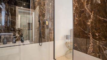 Un baño moderno con ducha de vidrio, paredes de mármol y tocador con artículos de aseo.