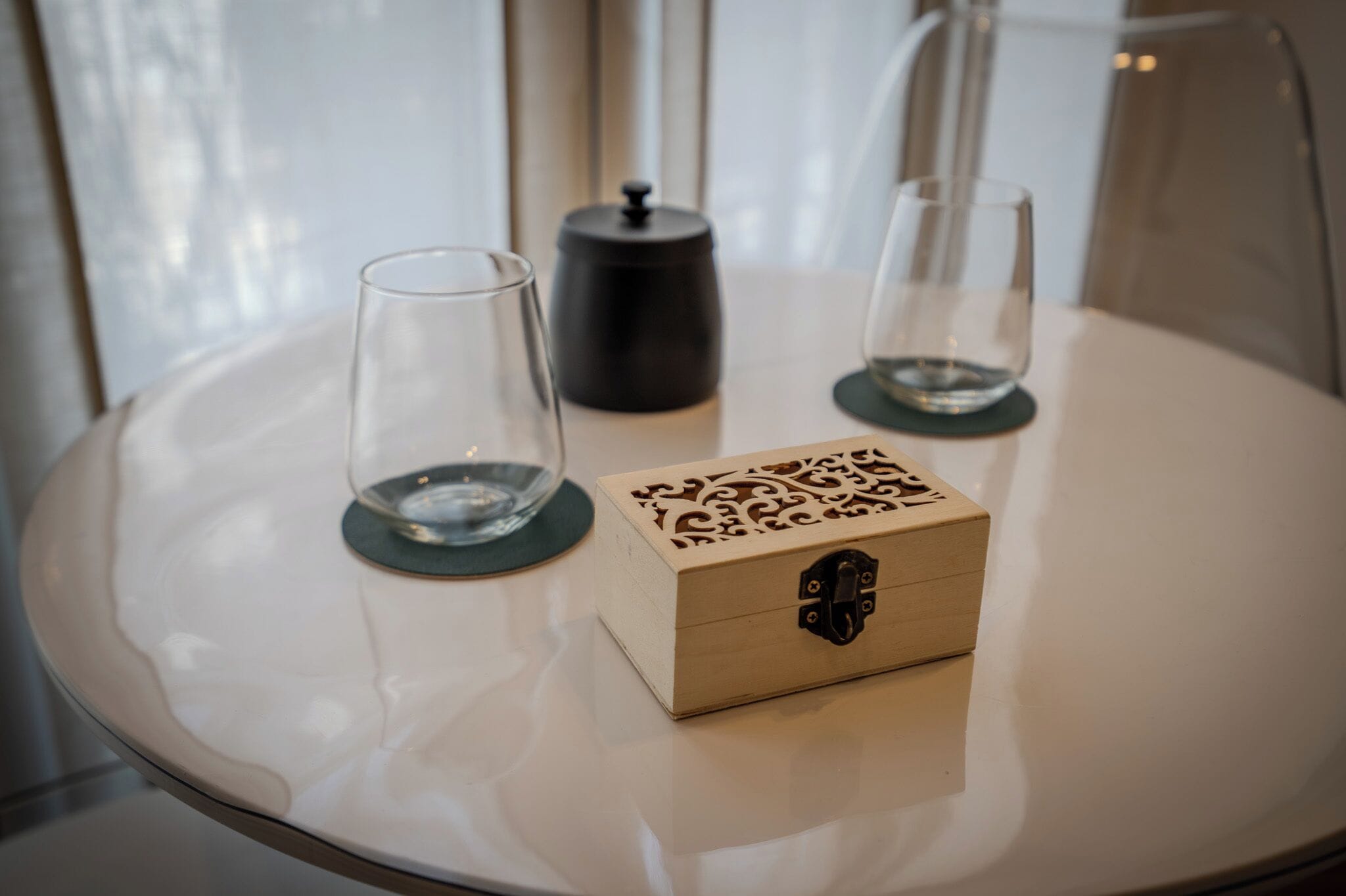 A round table with a wooden box and two glasses on coasters.