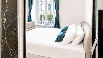 Um quarto com cama, janela com cortinas, varanda e vista para edifícios.