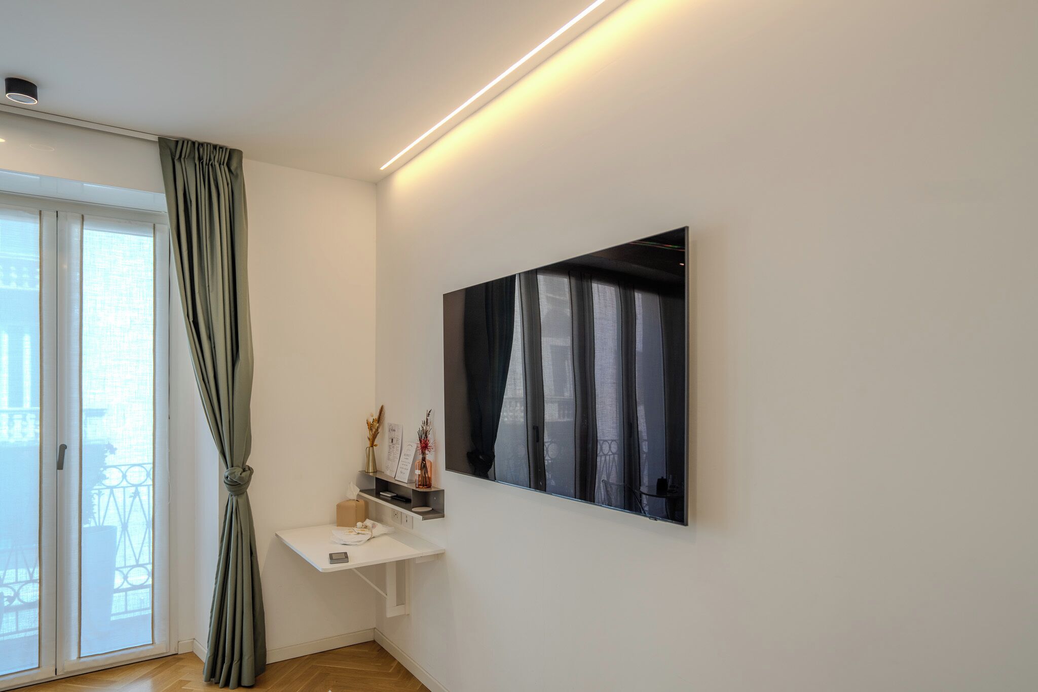 A modern room with a white desk, a large window with curtains, and a wall-mounted artwork.