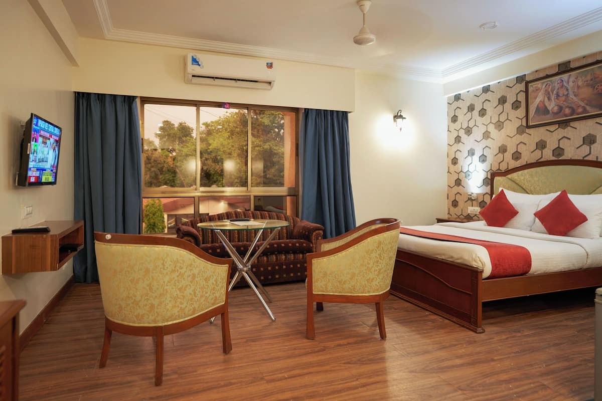 A hotel room with a bed, two chairs, a small table, a TV, and a window with curtains.