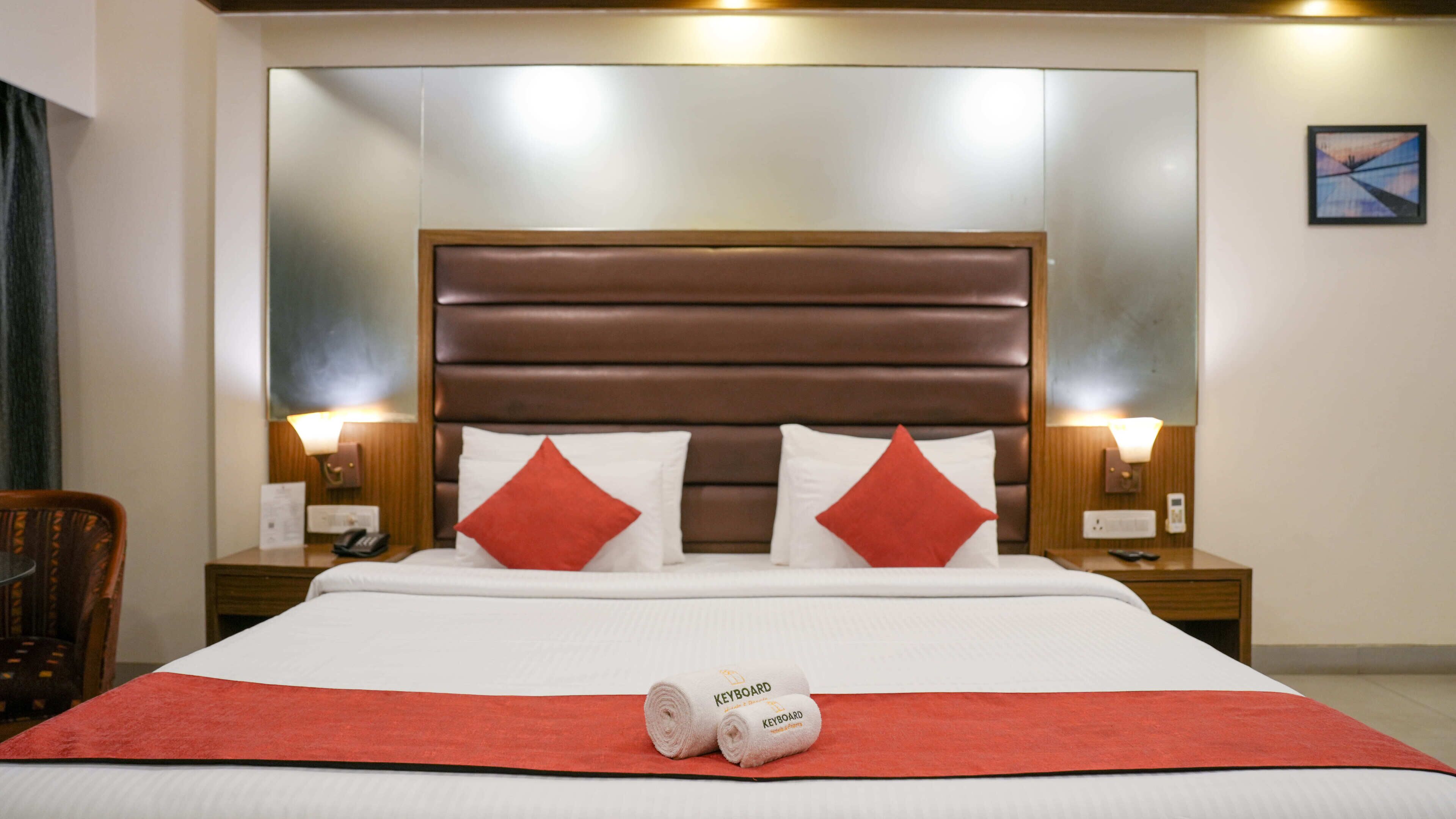 Una habitación de hotel con una cama grande, dos mesitas de noche, una manta roja y un cabecero con espejo.