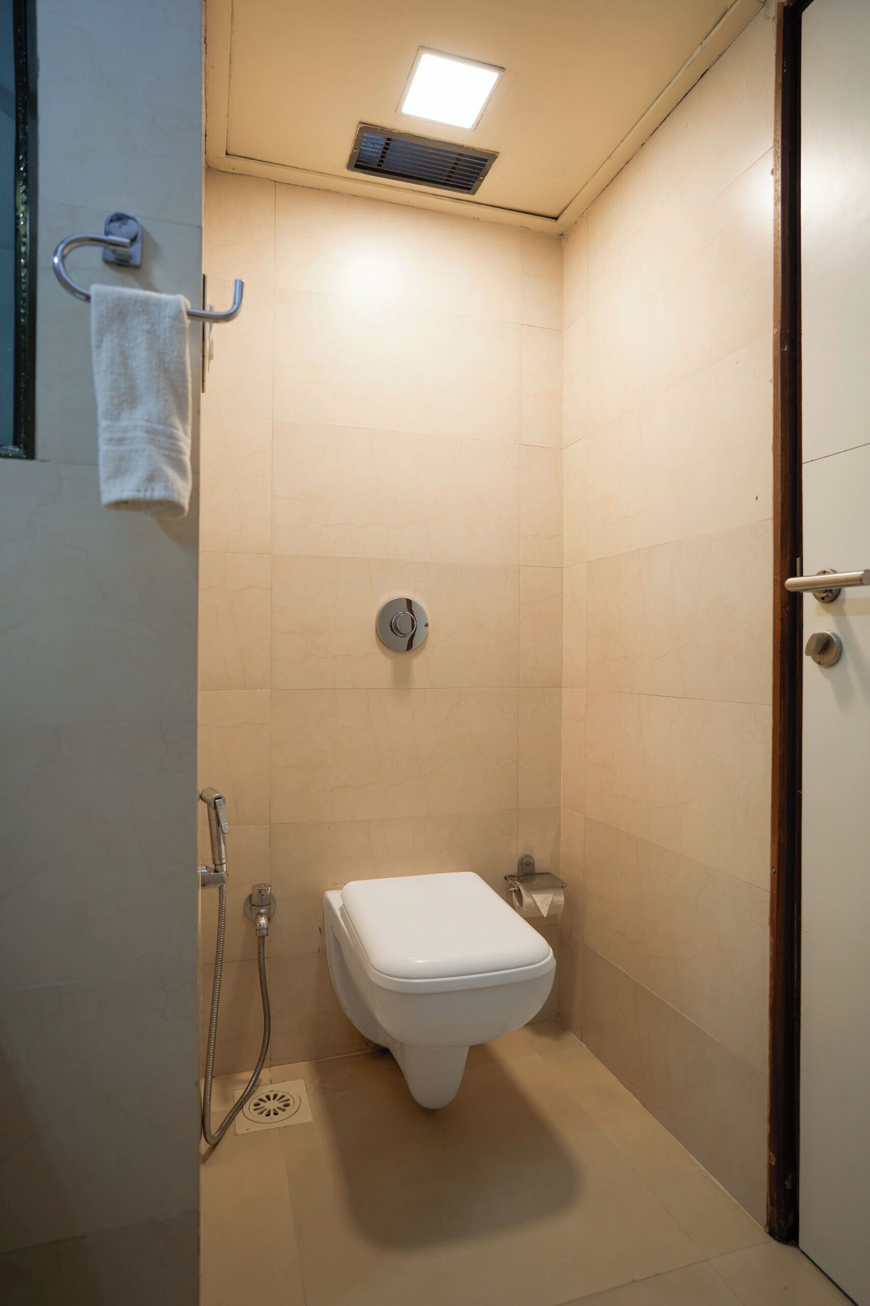 A small, enclosed bathroom with a toilet, a shower, and a towel rack.