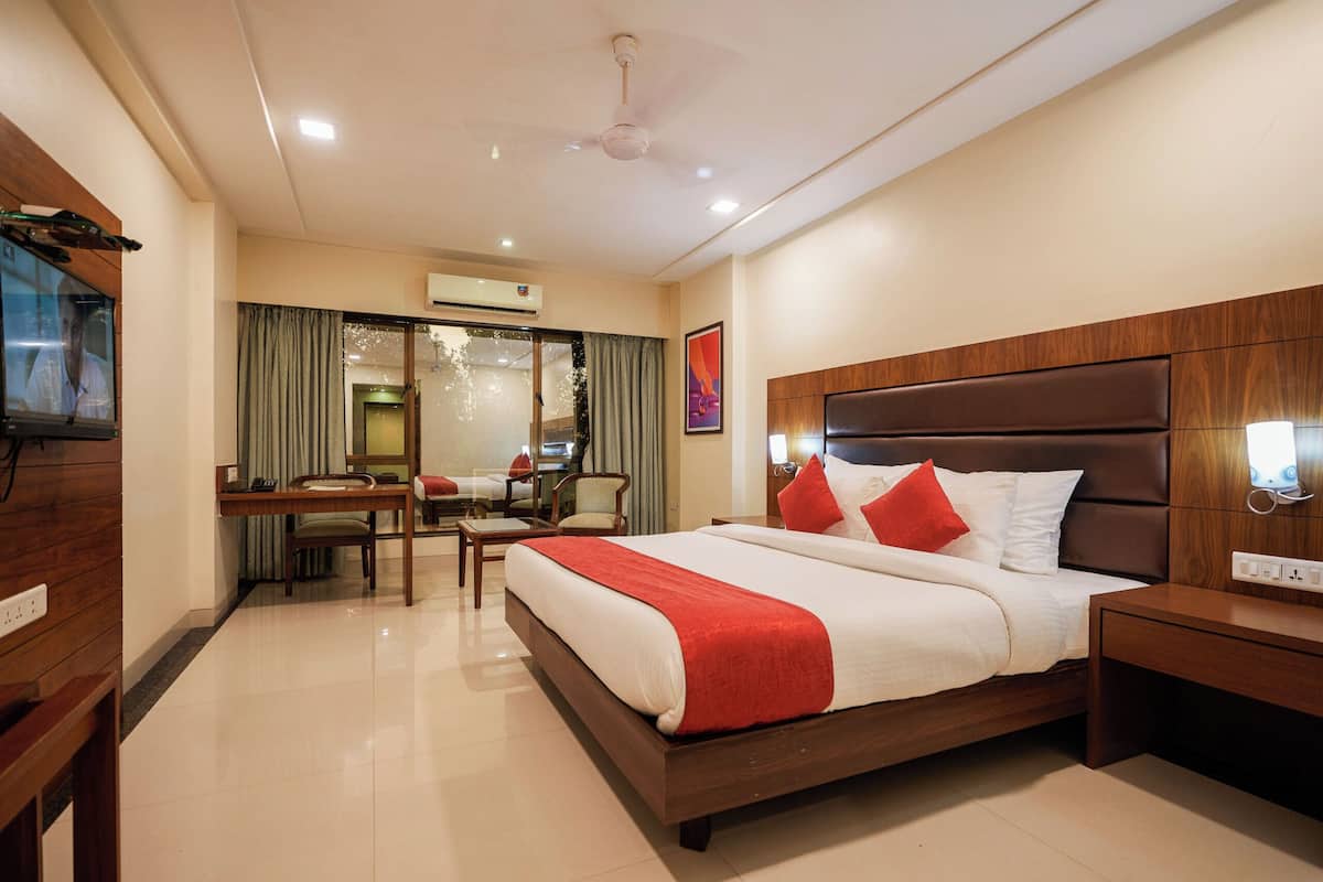 A hotel room with a large bed, a desk with a chair, a television, and a ceiling fan.