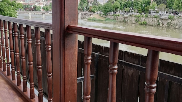 A wooden balcony railing overlooking a river with a town in the background. - Gönül sefası bütik otel  (Amasya)
