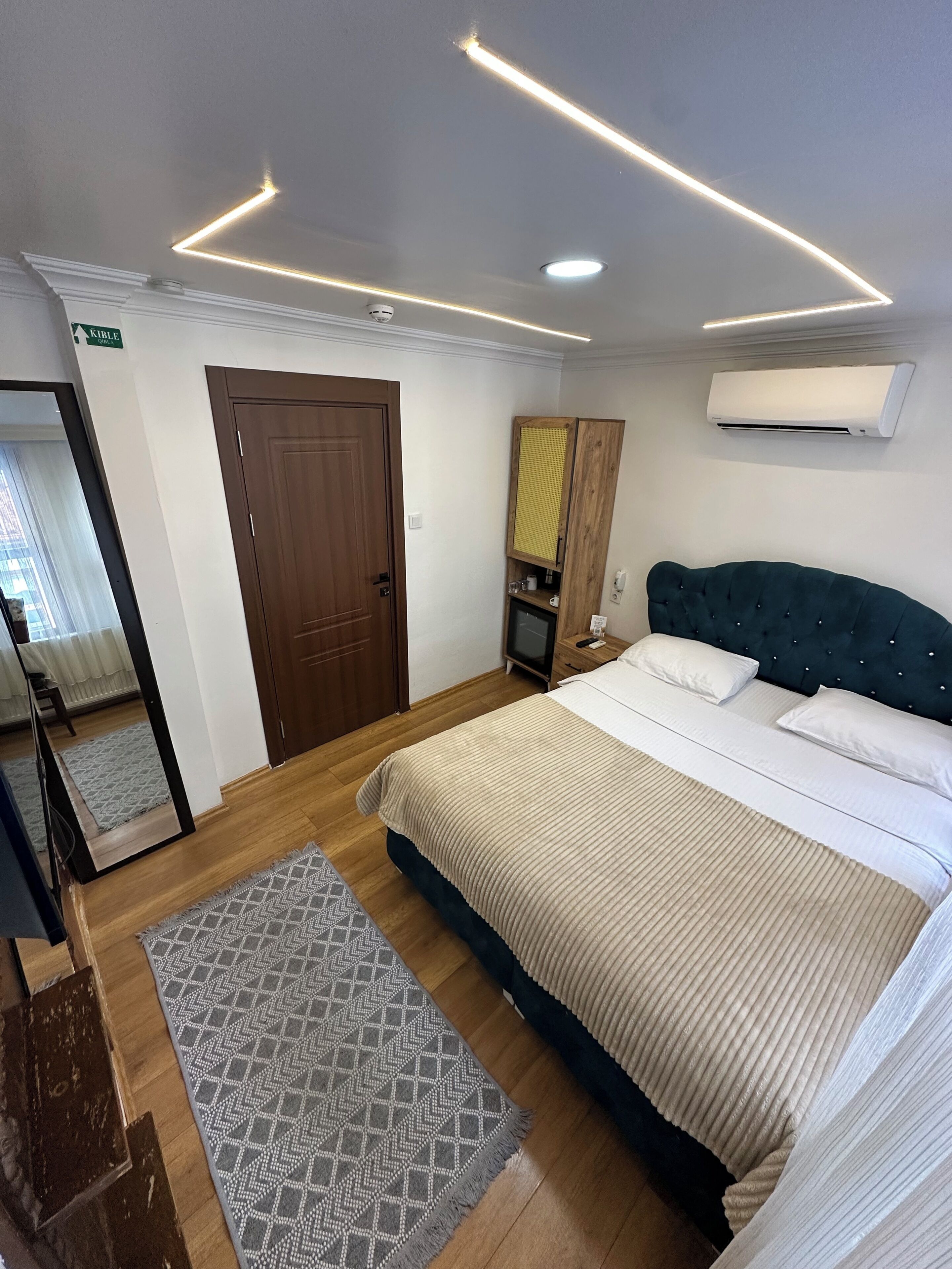 Een slaapkamer met een bed, een houten deur, een spiegel, een airconditioner en een kleine televisie.