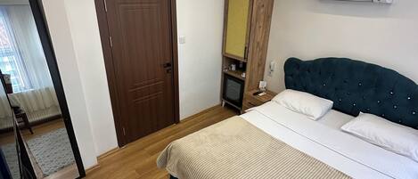 Een slaapkamer met een bed, een houten deur, een spiegel, een airconditioner en een kleine televisie.