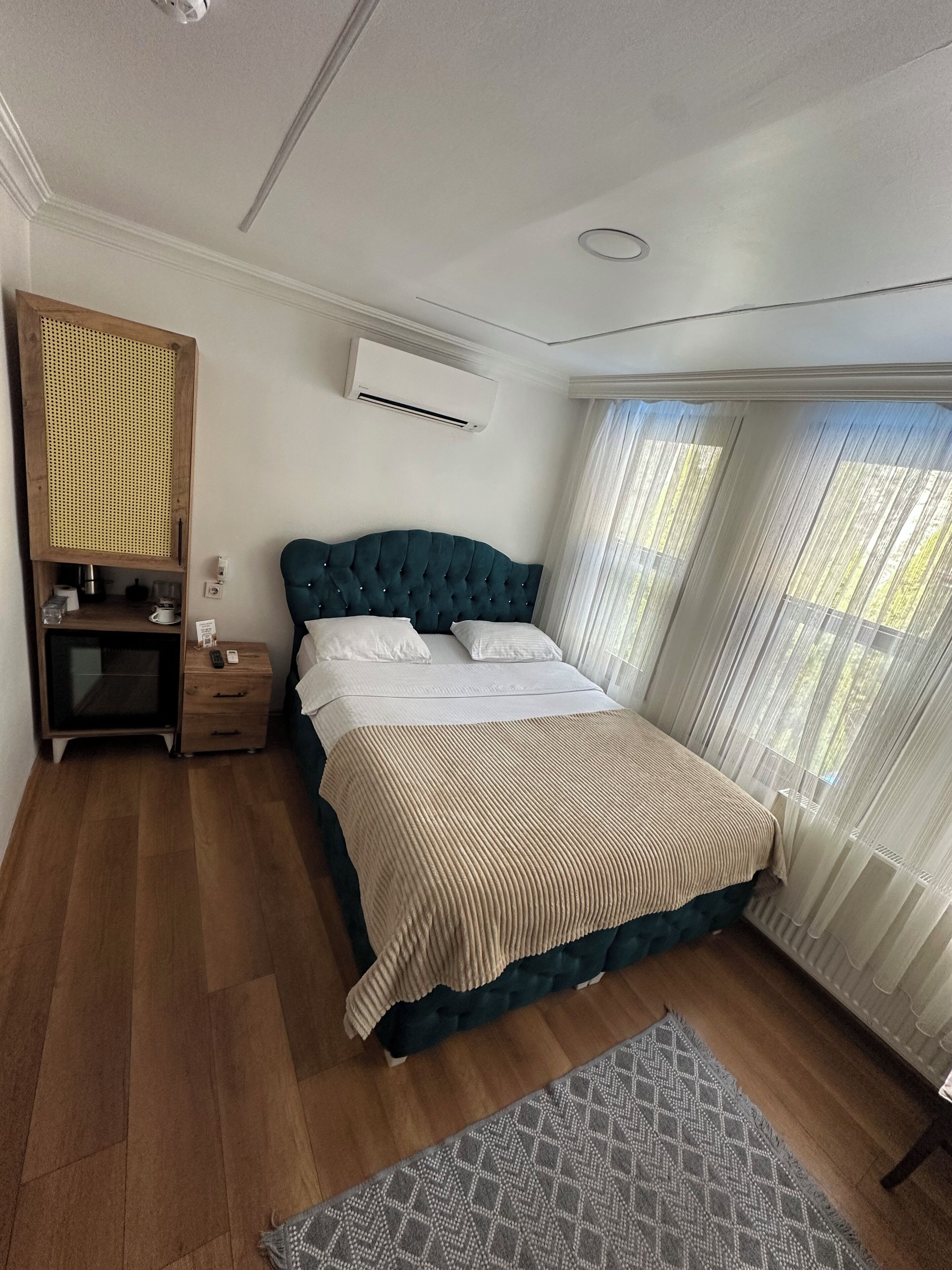 A bedroom with a bed, bedside table, nightstand, and a window with curtains.
